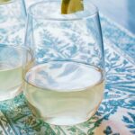 two glasses of fresh squeezed lemonade with lime wedges on table with blue white floral tablecloth