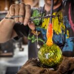 An artist's hands adds a loop to a green glass-blown holiday ornament in his studio glassblowing