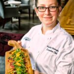 chef Kristin Beringson standing in restaurant holding a specialty food appetizer