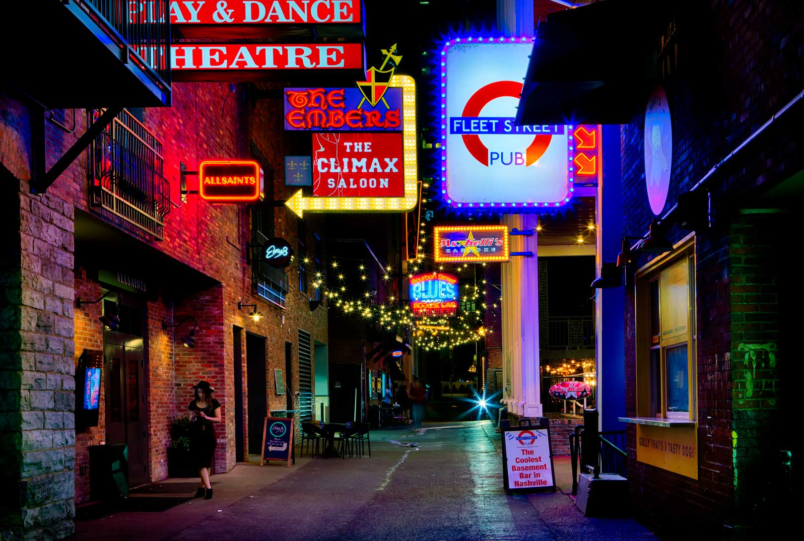 Bright signs of nightclubs lit up at night on old brick buildings along the Printers Alley district
