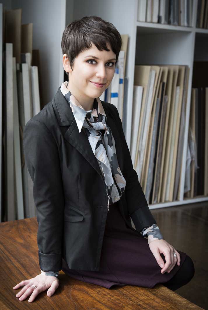Sara Estes sitting on a table in an art gallery in a black jacket with a floral scarf