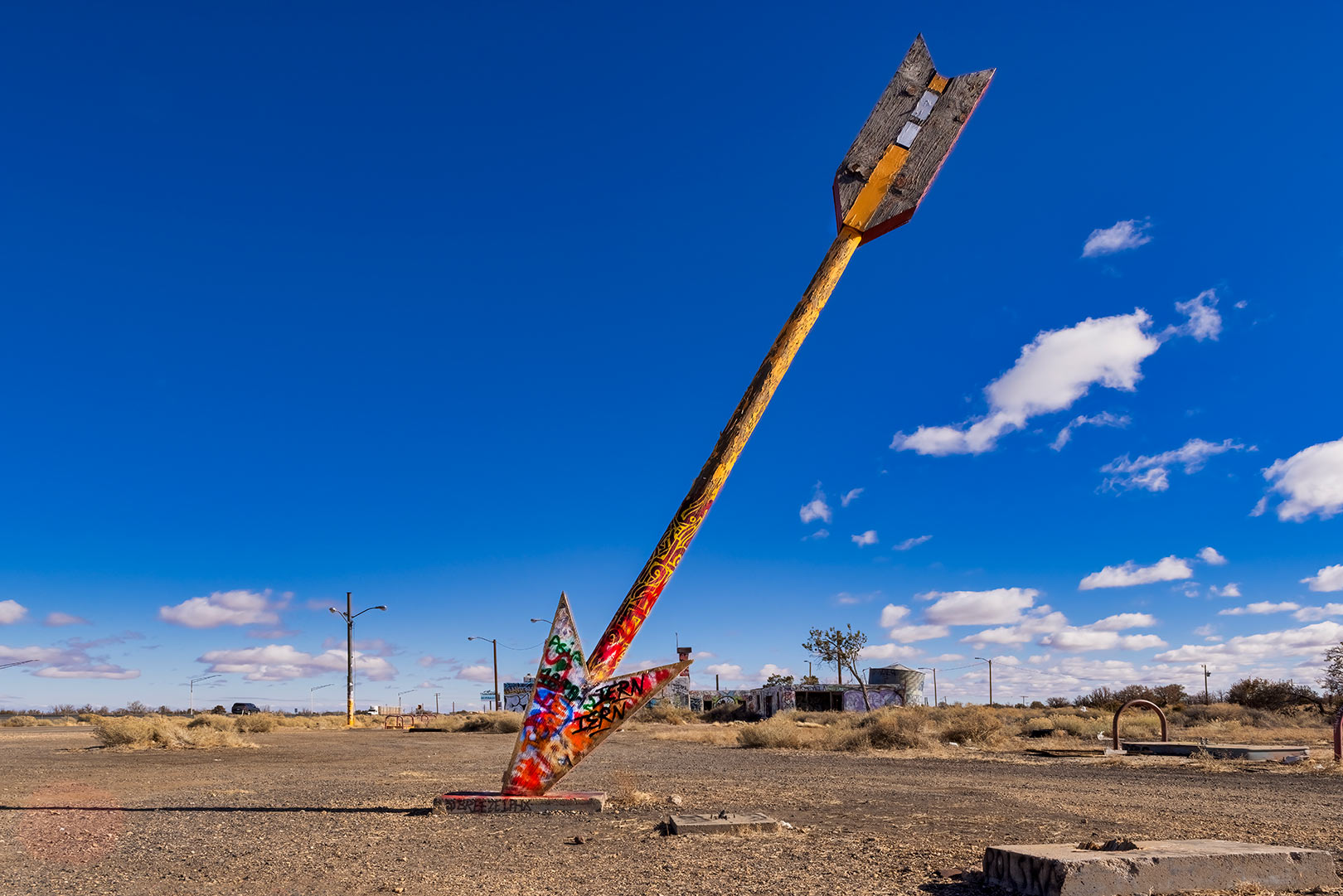 Large, colorful arrow at Twin Arrows Arizona stuck in the ground in a desert landscape under a clear blue sky.