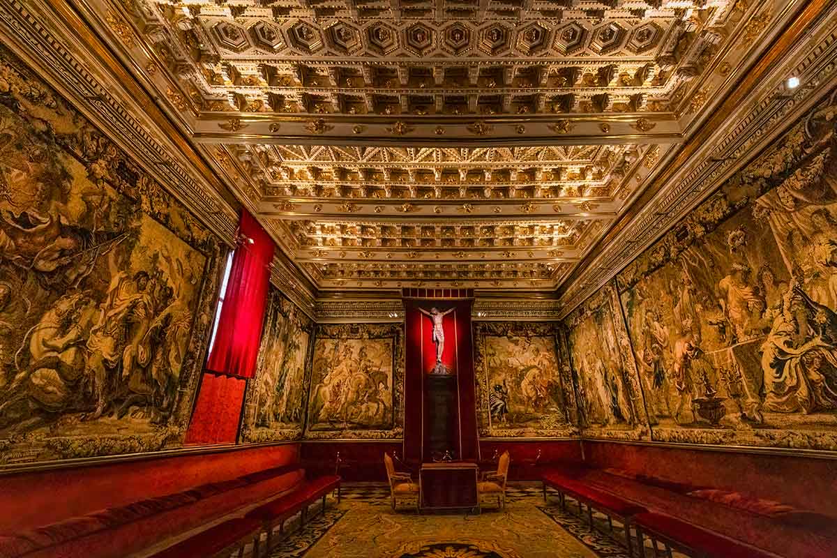 Jesus on the cross in a gold and red decor tapestry room at the Toledo Cathedral in Spain.