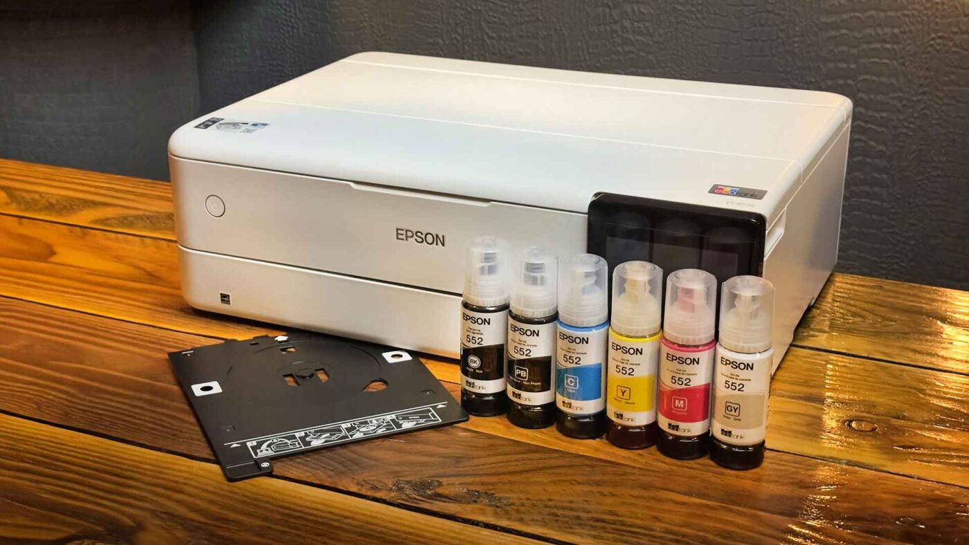 An Epson Ecotank ET-8550 printer sits on a wooden table next to five bottles of Epson ink and a black plastic tray, ready to unleash creativity in any workspace.