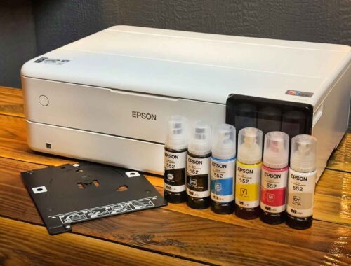 An Epson Ecotank ET-8550 printer sits on a wooden table next to five bottles of Epson ink and a black plastic tray, ready to unleash creativity in any workspace.