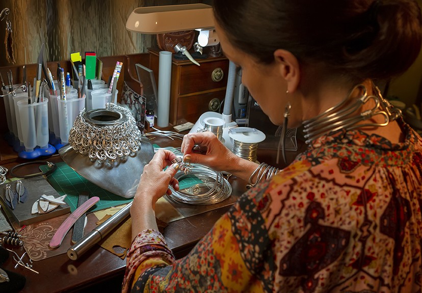 Jewelry artist Mary Elizabeth Long sitting at a table bending wire into spiral shapes by hand to make a necklace